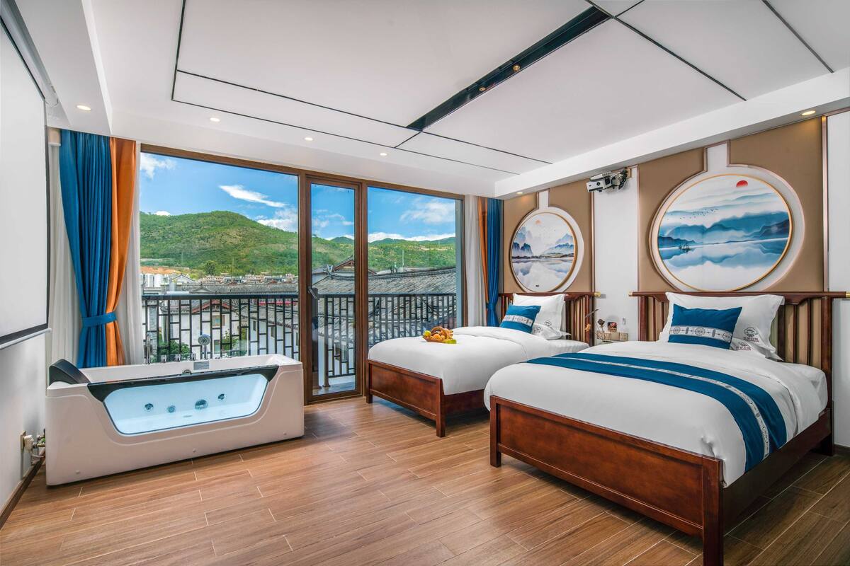 A hotel room with two beds, a bathtub, and a balcony with a scenic view.