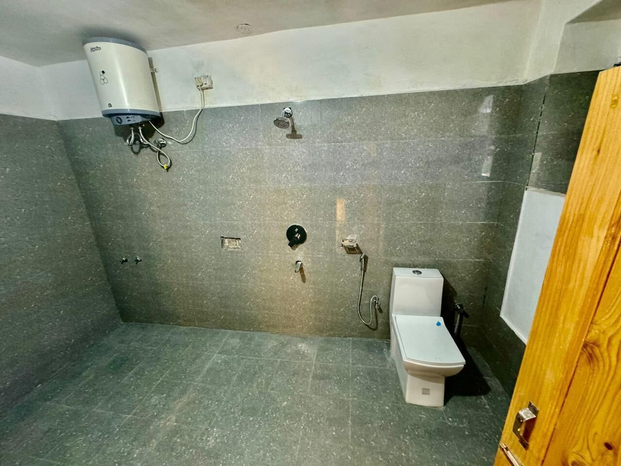 A small, tiled bathroom with a toilet, a shower, and a water heater.