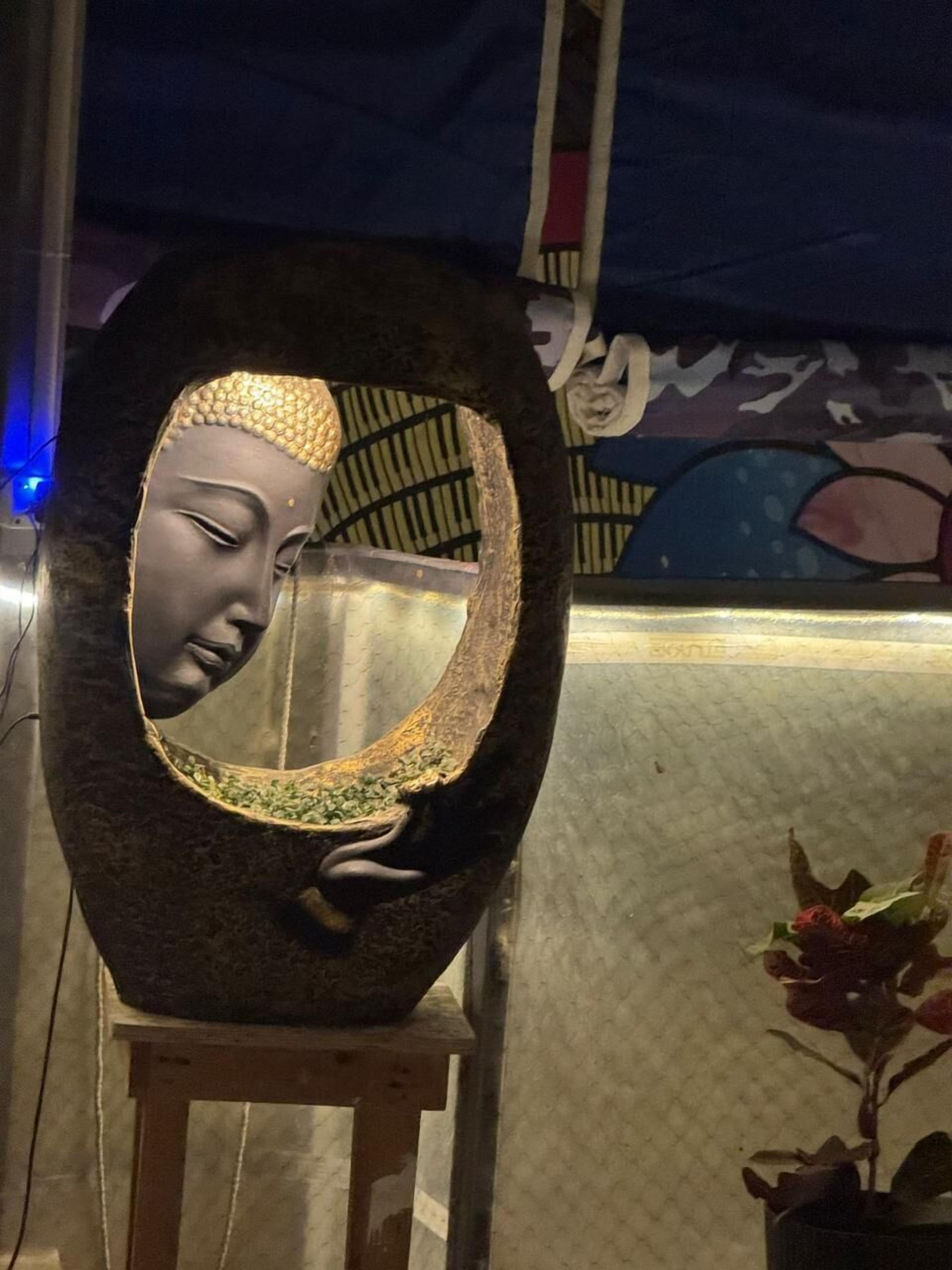 A sculpture with a face, a wooden stool, and a potted plant.