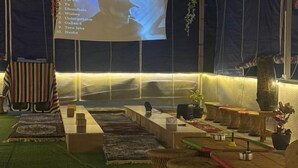 Ett mysigt loungeområde med en projektionsduk som visar en lista över låtar, bekväma sittplatser och ett grönt, mattbeklätt golv.
