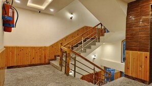 A staircase with wooden railings and granite steps, leading to a landing with a wooden wall and a glass elevator door. - Hotel Shingar - Sunrise Hotel & Resorts (Bhuntar)