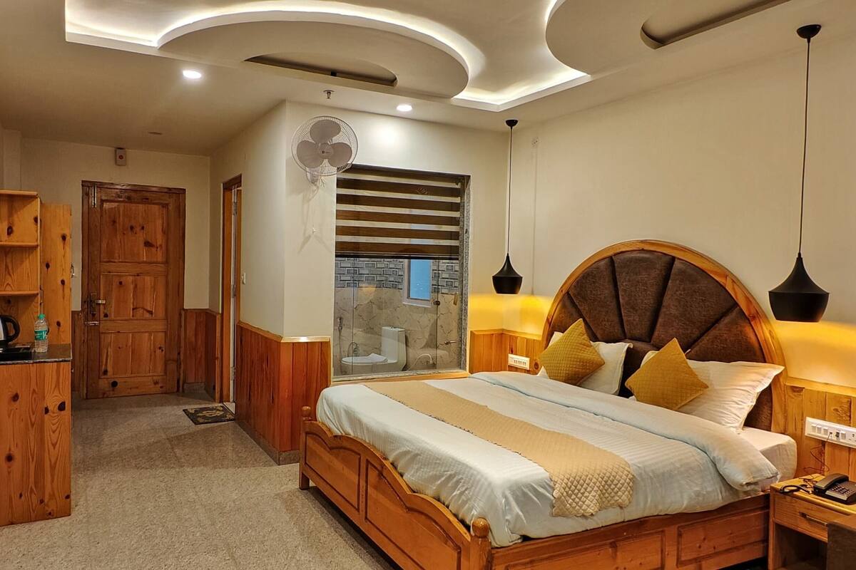 Une chambre avec un lit en bois, des lampes de chevet, une armoire en bois et une salle de bain visible à travers une porte en verre.