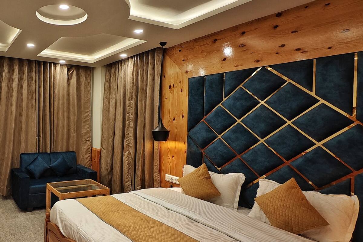 Une chambre à coucher avec un lit, une tête de lit en bois, un fauteuil bleu, une armoire en bois et une grande fenêtre avec des rideaux.
