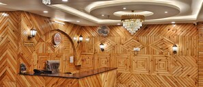 Un área de recepción con un revestimiento de madera en patrón de espiga, una mesa de recepción, una araña y luces de pared.
