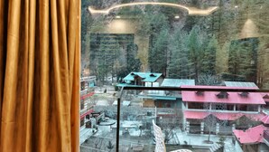 A view from a window with curtains, overlooking a mountainous area with buildings and trees. - Hotel Shingar - Sunrise Hotel & Resorts (Bhuntar)