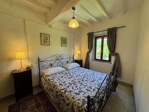 Une chambre à coucher avec un lit, deux lampes de chevet, une fenêtre avec des rideaux et un luminaire suspendu.