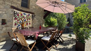 An outdoor patio with a table and chairs, a large umbrella, a stone wall, and a mural. - L'Antico Palazzo - Mansion with Pool (TOANO)