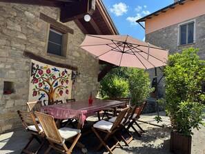 An outdoor patio with a table and chairs, a large umbrella, a stone wall, and a mural. - L'Antico Palazzo - Mansion with Pool (TOANO)