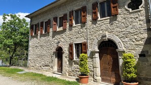 A stone building with multiple windows and doors, a small garden area with potted plants, and a clear blue sky. - L'Antico Palazzo - Mansion with Pool (TOANO)