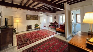 A spacious living room with a large red carpet, wooden beams on the ceiling, a sofa, a chair, and a lamp. - L'Antico Palazzo - Mansion with Pool (TOANO)