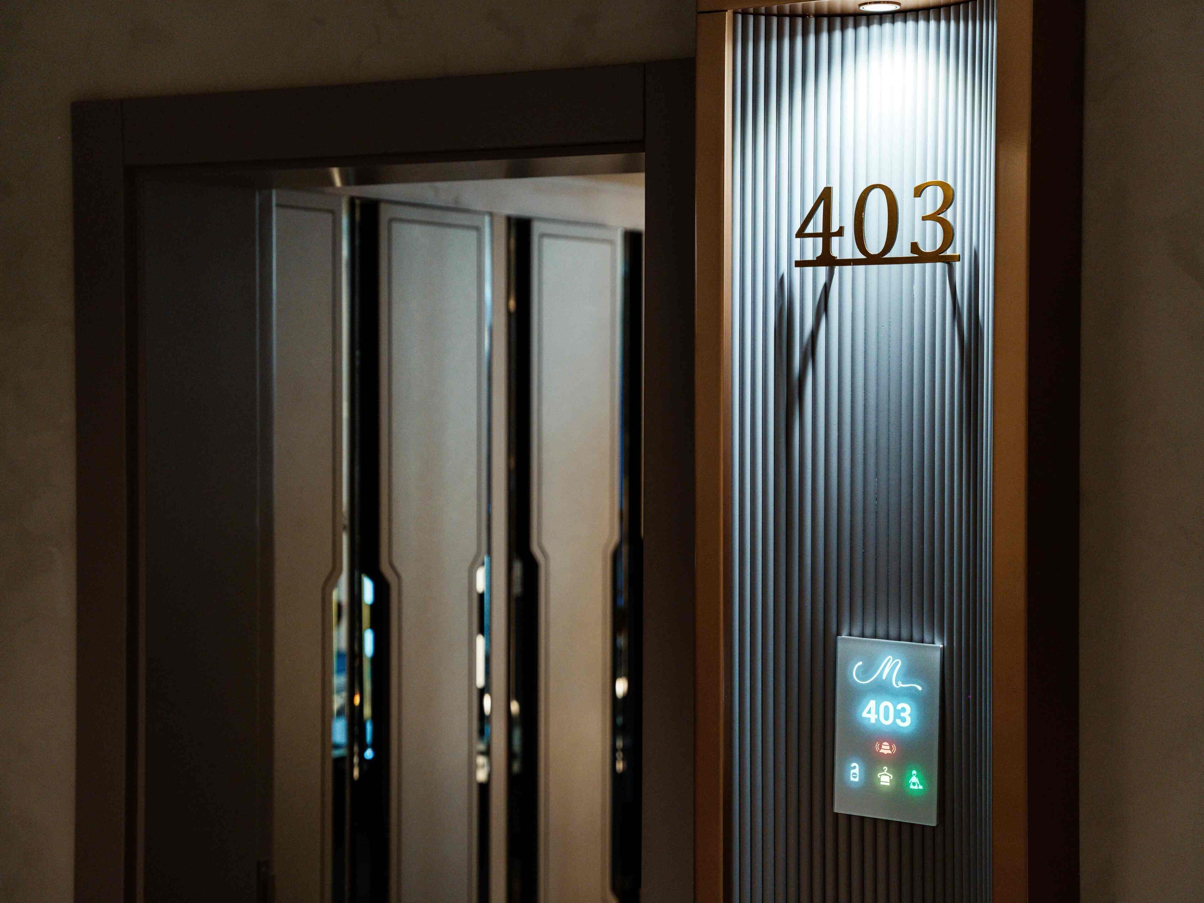 Entrada de hotel con un letrero metálico con el número '403' y una pantalla digital que muestra los servicios de las habitaciones.