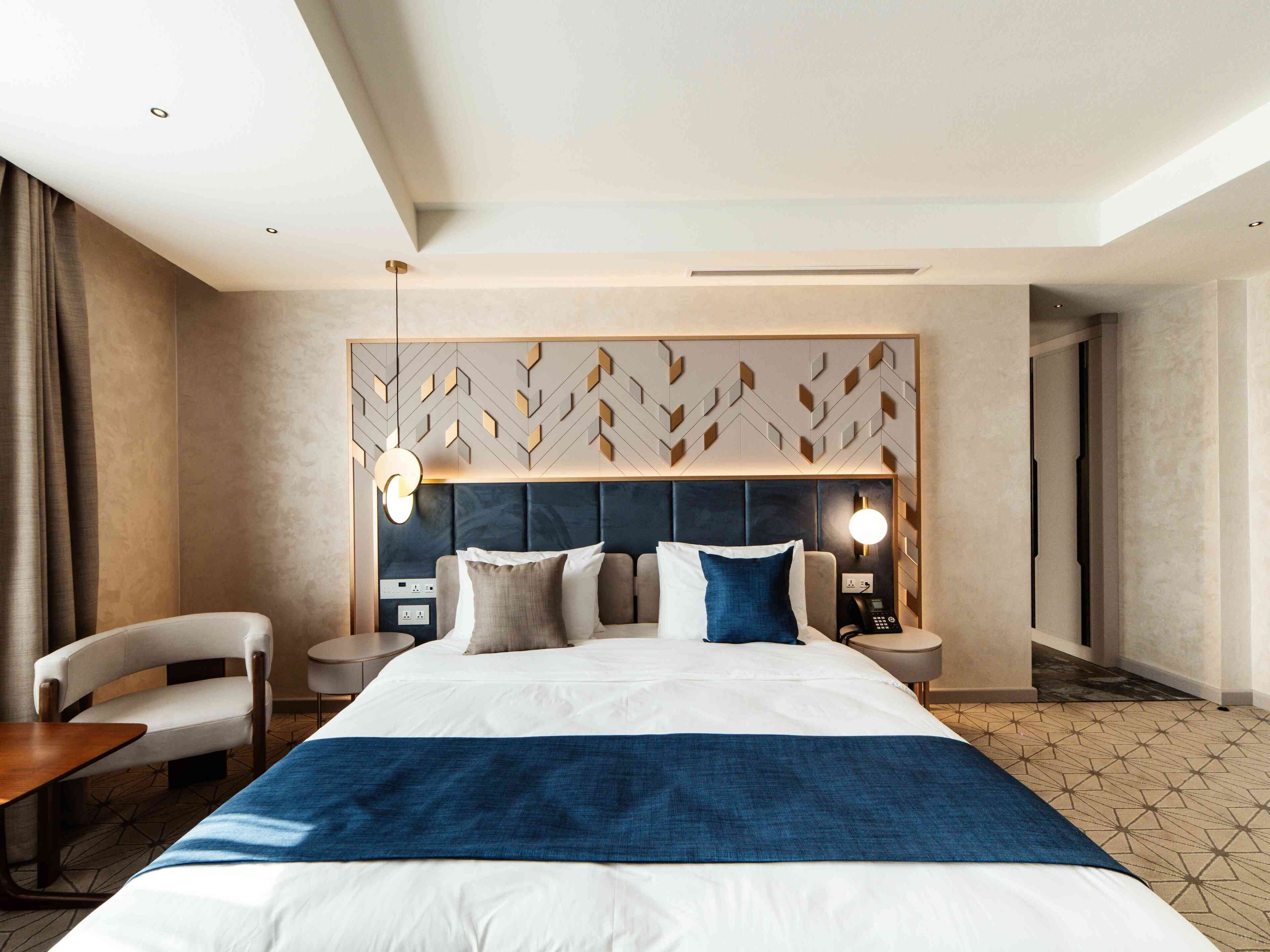 Een hotelkamer met een groot bed, een bureau, een stoel, een nachtkastje en een aan de muur bevestigd telefoon.