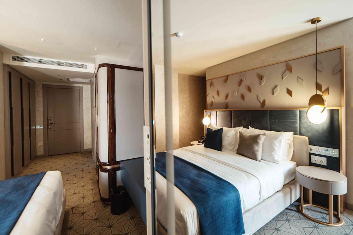 A hotel room with a large bed, bedside tables, a desk, and a modern light fixture.