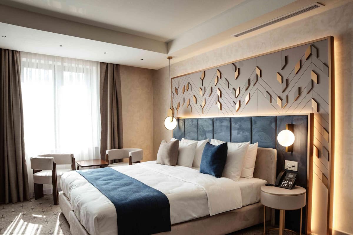 A hotel room with a bed, bedside table, lamp, and a chair.