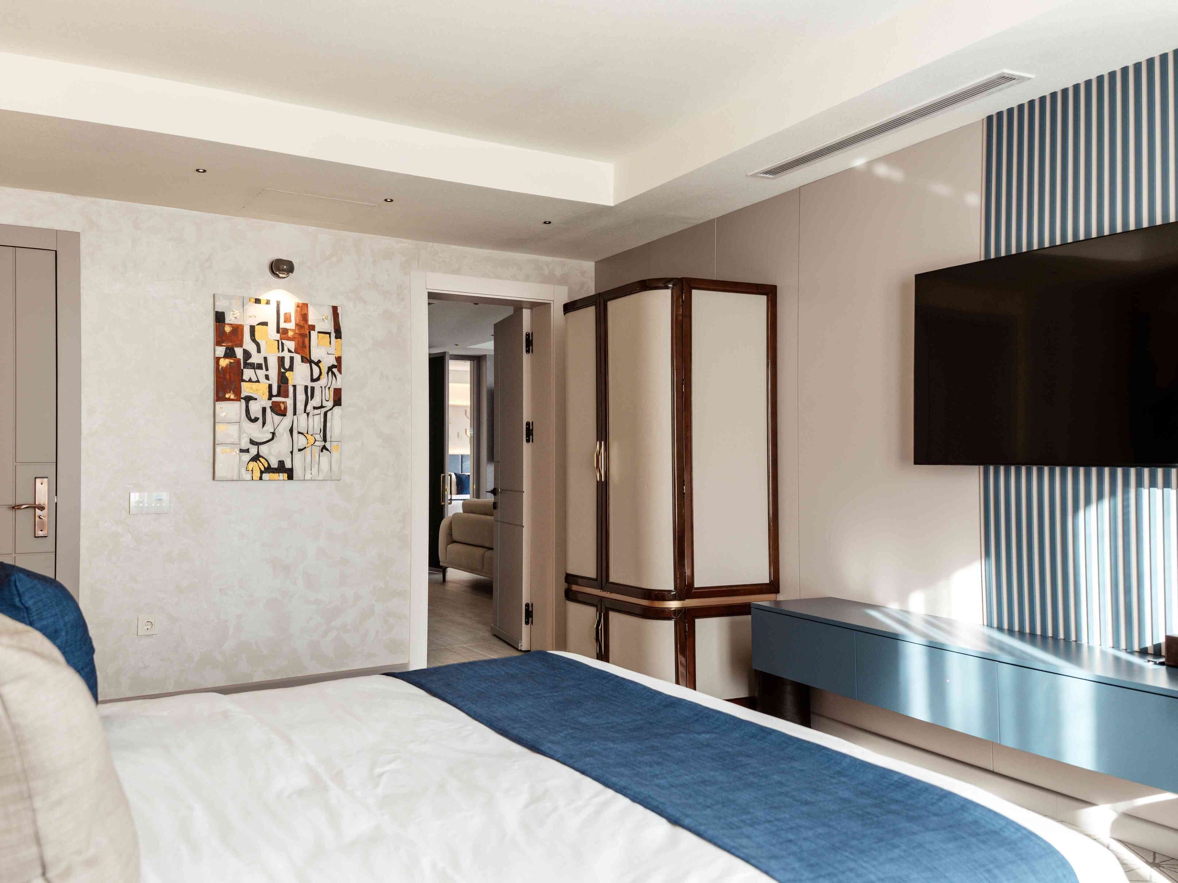 Una habitación de hotel moderna con cama, televisor, armario y un cuadro en la pared.