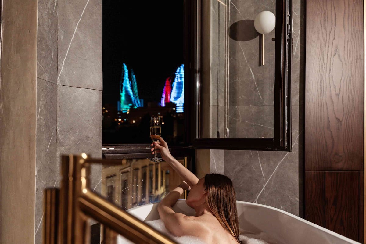A person in a bathtub with a view of illuminated buildings outside.