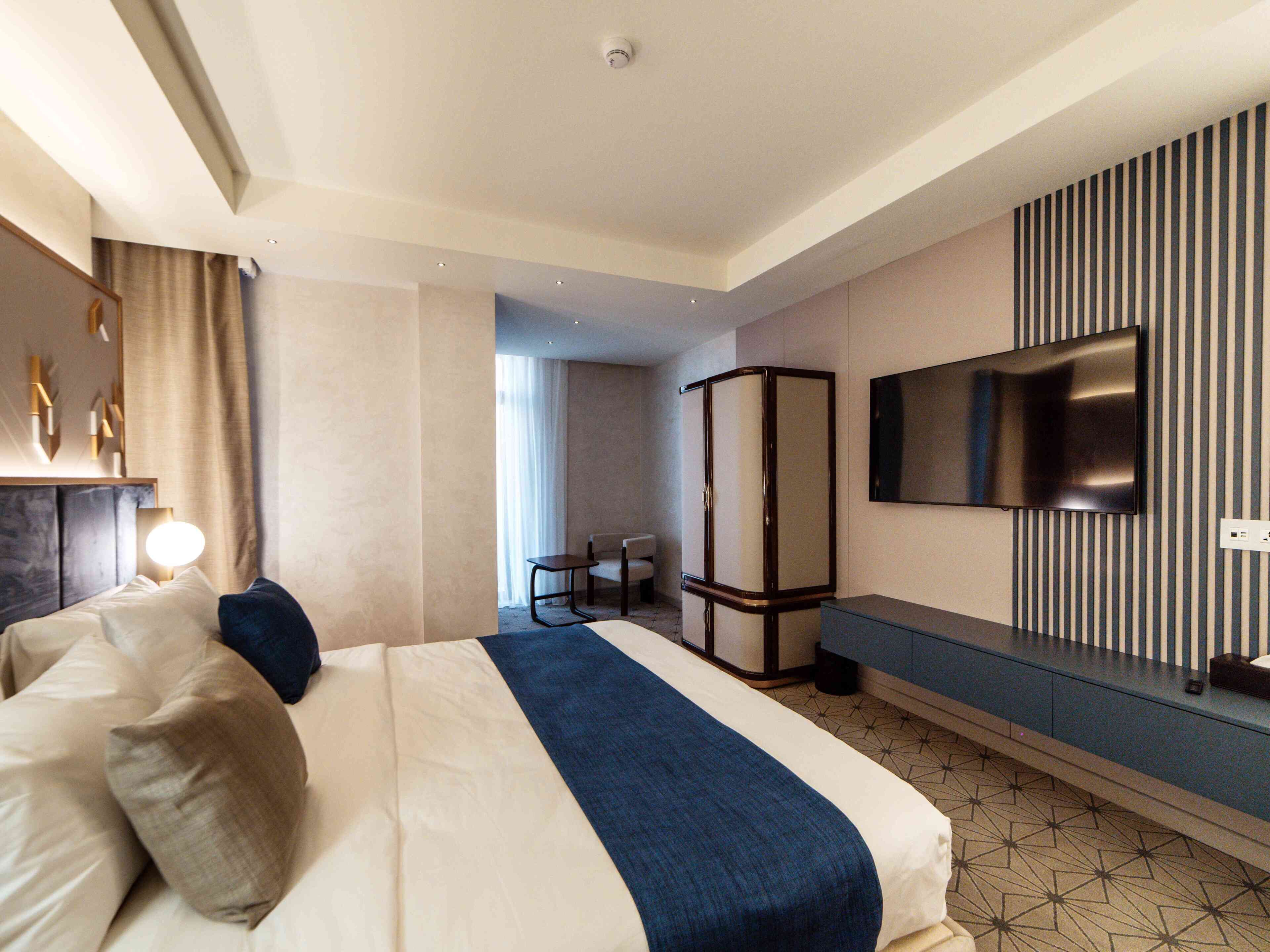 Habitación de hotel con cama, televisión, armario y baño visible a través de una puerta abierta.