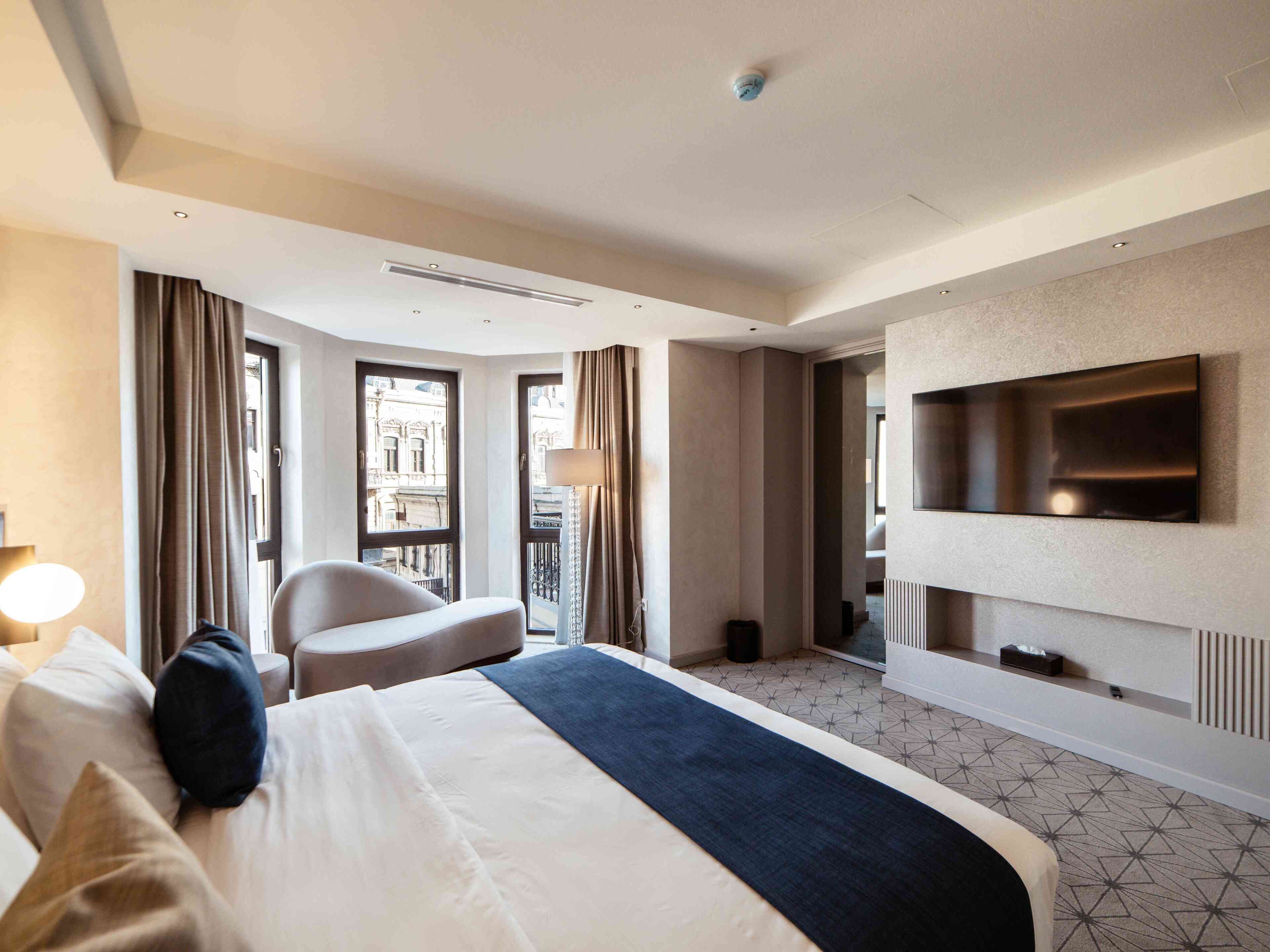 Ein Hotelzimmer mit Bett, Sessel, Fernseher und Blick auf die Stadt.