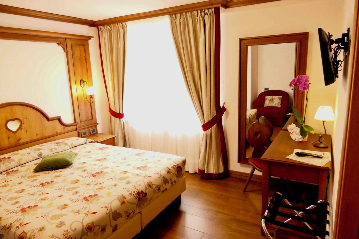 A hotel room with a bed, a desk, a chair, a TV, and a window with curtains.