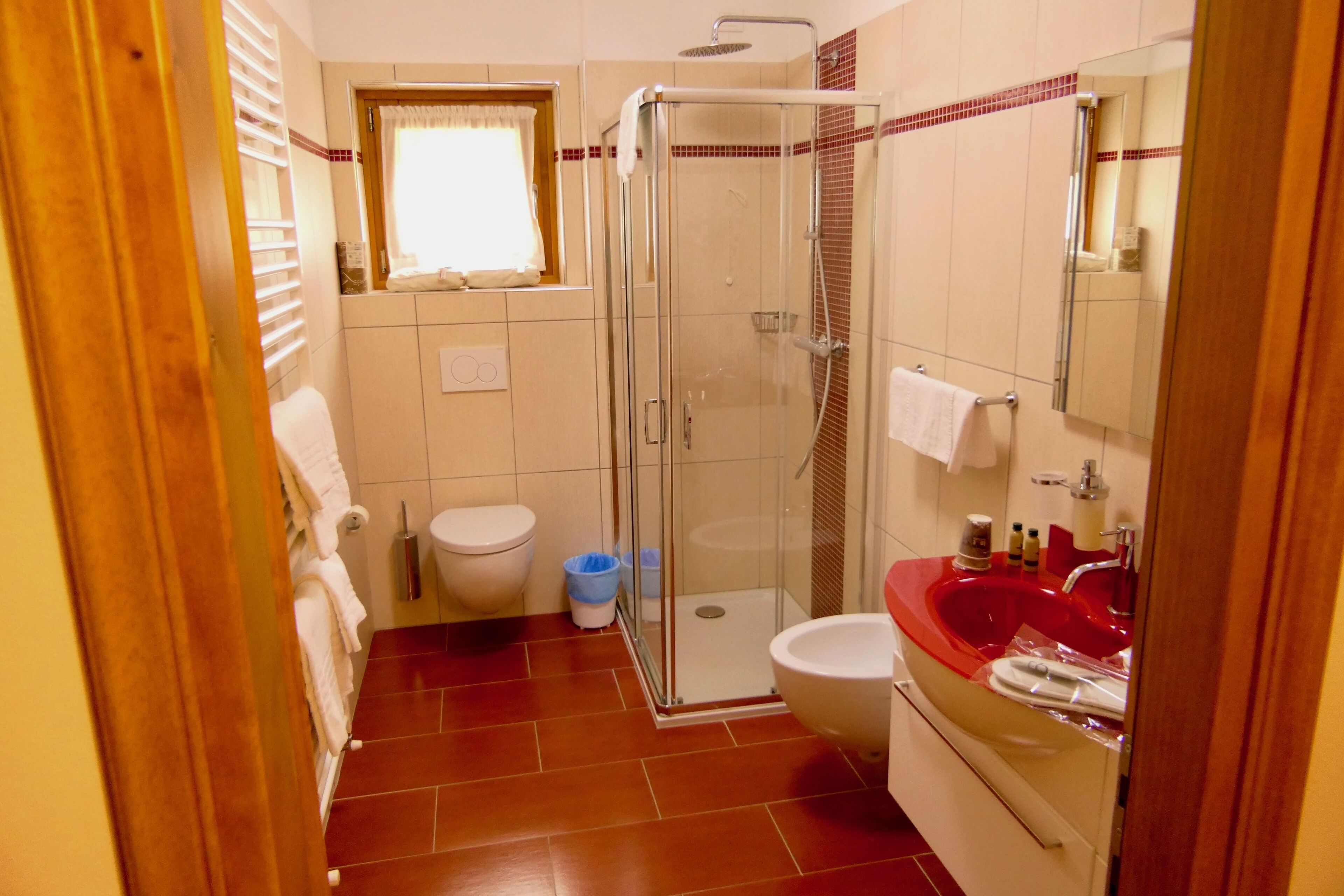 A bathroom with a glass-enclosed shower, a red sink, and a white toilet.