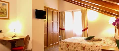 A bedroom with a wooden desk, chair, bed with floral bedding, and a TV mounted on the wall.