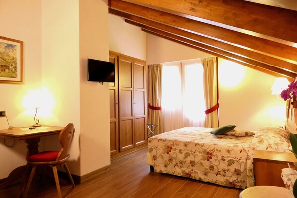 A bedroom with a wooden desk, chair, bed with floral bedding, and a TV mounted on the wall.