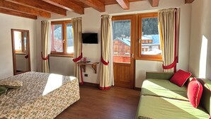 A room with wooden beams on the ceiling, a bed with floral bedding, a sofa with red cushions, and a window with curtains. - Dream hotel  (Staffa)