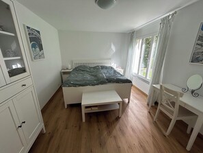 A bedroom with a bed, a desk, a chair, a wardrobe, and a window with curtains.