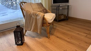 Une pièce chaleureuse avec un fauteuil en osier, un téléviseur posé sur une table en verre et une vue sur un paysage enneigé par la fenêtre.