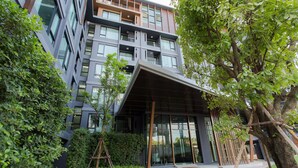Edifici modern amb façana de vidre, entrada coberta i vegetació als voltants.