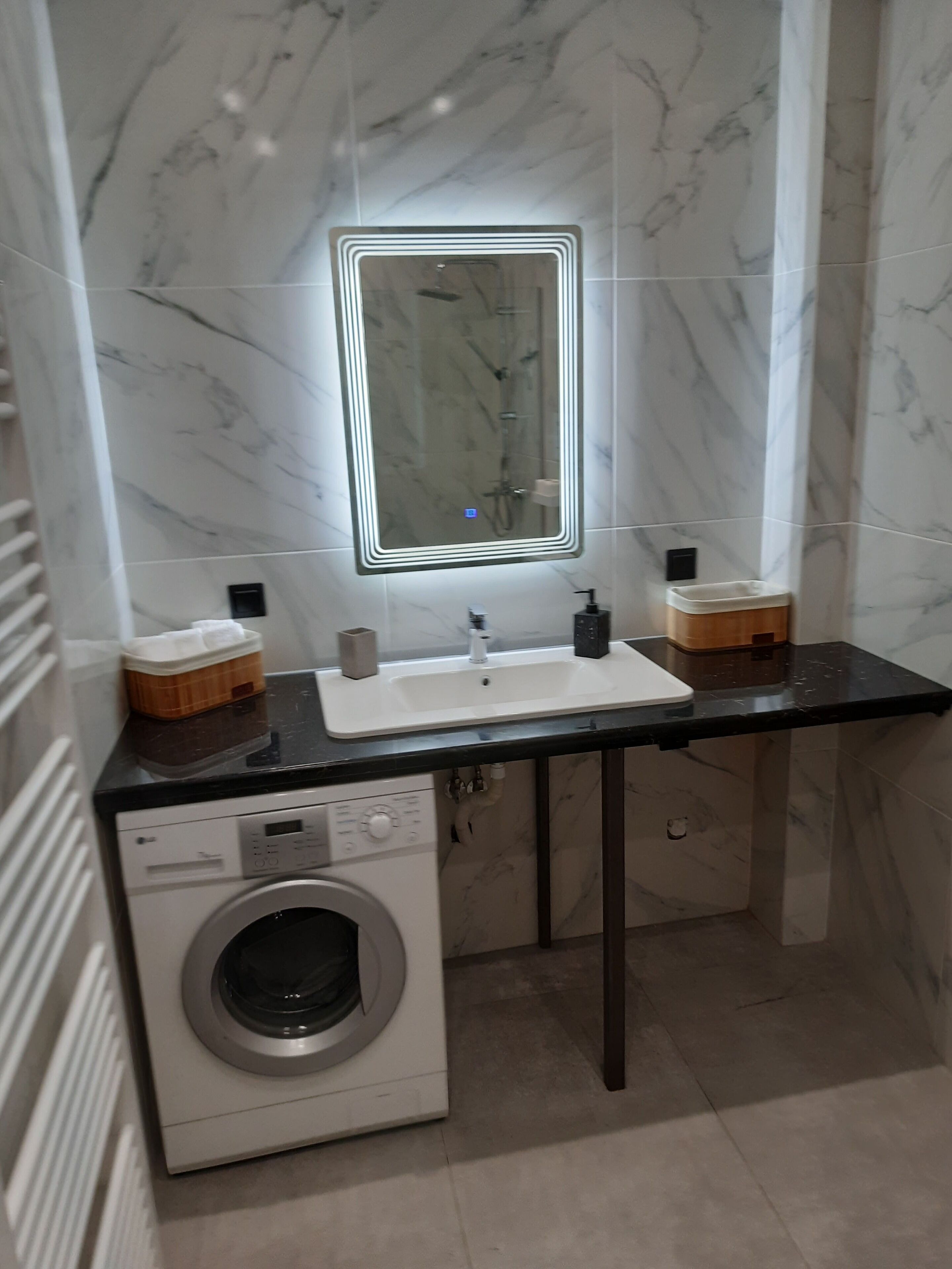 Een moderne badkamer met een marmeren spatwand, een ingebouwd wastafelmeubel, een spiegel, een wasmachine en een klein houten kastje.