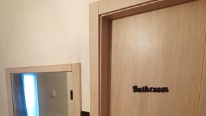A wooden door with a sign reading "Bathroom" and a hallway leading to a room with a table and chairs.