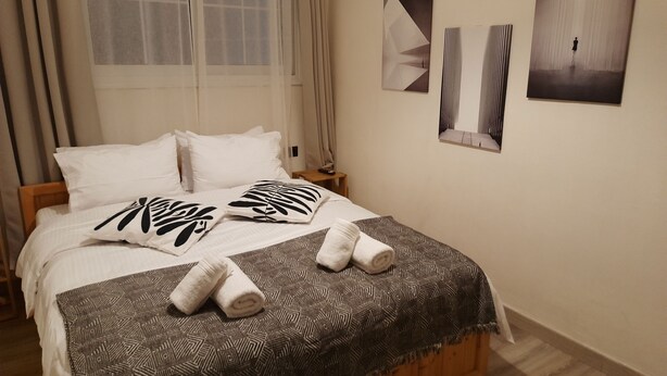 A neatly made bed with patterned pillows and a geometric throw blanket, a bedside table with a lamp, and abstract wall art.