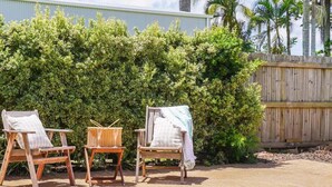 A pool area with two wooden chairs and a small table, surrounded by dense green foliage and a wooden fence. - Welcome to "Bay 13" The Perfect Family Retreat with Inground Pool (Tin Can Bay)