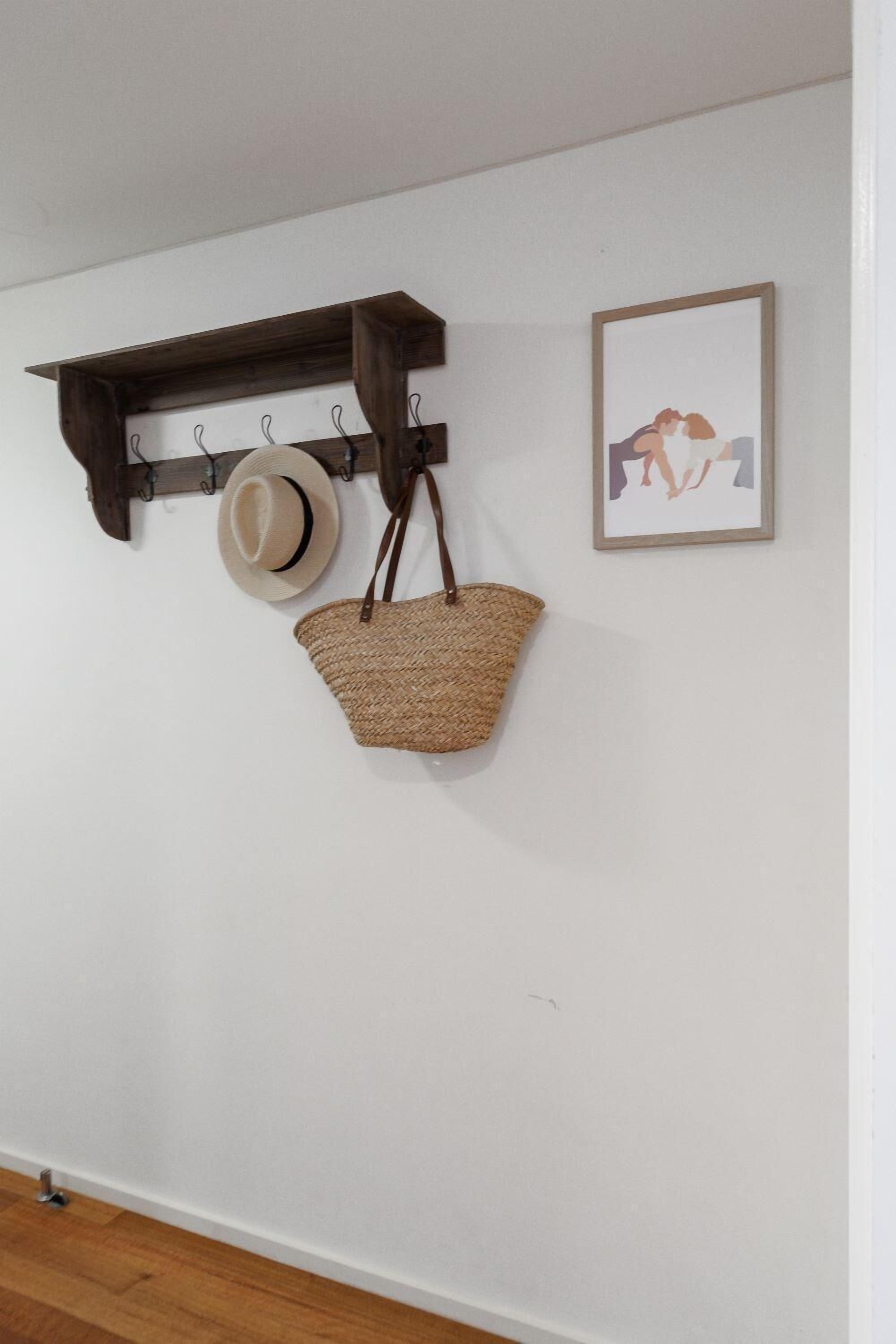 A wall-mounted wooden shelf with a hat and a woven basket hanging from it.