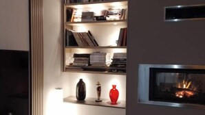 A modern living room with a fireplace, bookshelves, and a flat-screen TV. - Room at Sylvie's, breakfast included (Val-d'Izé)