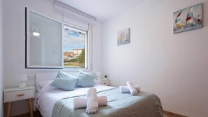A hotel room with a bed, a nightstand, a window, and a painting on the wall. - Golden Coast Retreat by Fidalsa (Creixell)