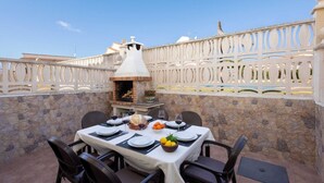 An outdoor dining area with a stone wall, a white decorative fence, and a pizza oven. - Golden Coast Retreat by Fidalsa (Creixell)