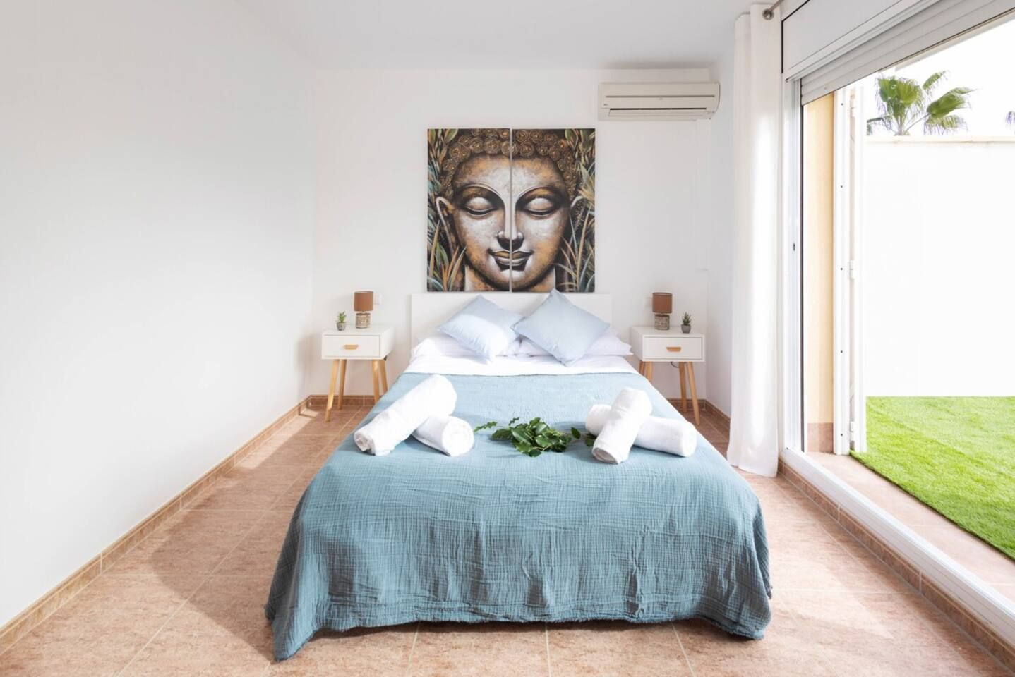 Un dormitorio con cama, dos mesitas de noche, una obra de arte grande en la pared y vistas al exterior.