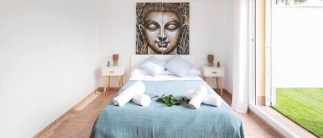 Un dormitorio con cama, dos mesitas de noche, una obra de arte grande en la pared y vistas al exterior.