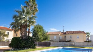 A swimming pool with a clear blue water, surrounded by a fence, palm trees, and a building with a tiled roof. - Golden Coast Retreat by Fidalsa (Creixell)