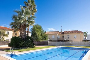 Une piscine à l’eau d’un bleu cristallin, entourée d’une clôture, de palmiers et d’un bâtiment doté d’un toit en tuiles.