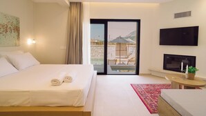 A modern hotel room with a large bed, a flat-screen TV, a balcony with outdoor seating, and a view of the mountains. - Atman Eco Lodge (Souli)