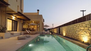 A modern outdoor pool area with a stone wall, lounge chairs, and a well-lit patio. - Atman Eco Lodge (Souli)