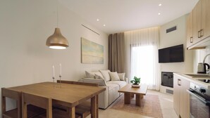 A modern living room with a wooden dining table, sofa, and a TV mounted on the wall. - Atman Eco Lodge (Souli)