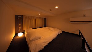 A hotel room with a bed, a bedside table, an air conditioning unit, and a window with curtains. - Apartment Sanjo (Nara)