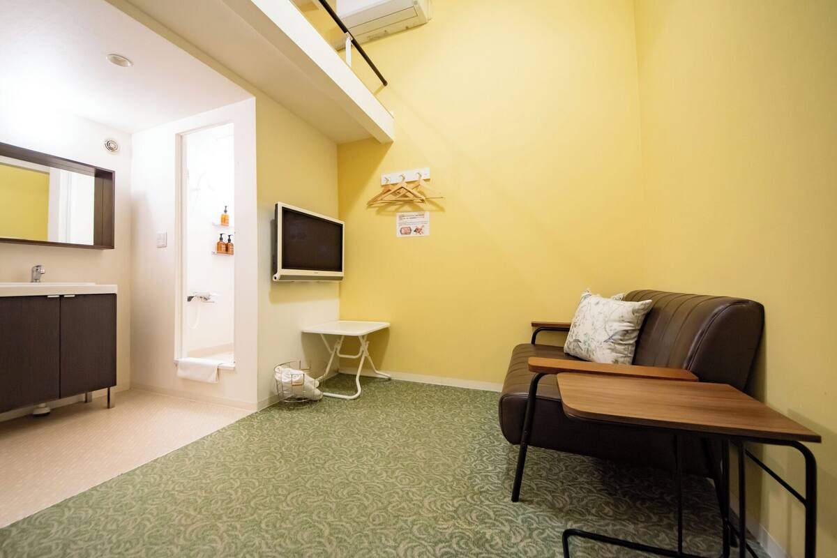 A small, compact room with a kitchenette, a single bed, a TV, and a wall-mounted drying rack.