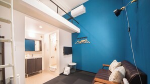 A room with a blue wall, a wooden sofa, a TV, and a ceiling-mounted lamp. - Apartment Sanjo (Nara)
