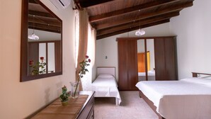 A bedroom with two single beds, a wooden wardrobe, a dresser, a mirror, and a cactus plant.