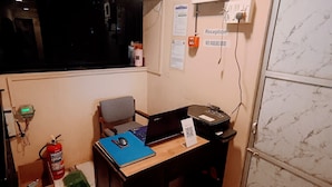 A small office with a desk, computer, and chair. There is a fire extinguisher, a window, and a door. - Marol nandham dormitory  (Mumbai)